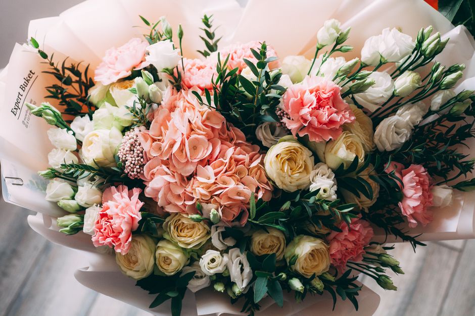 A meticulously arranged bouquet featuring soft pink hydrangeas, creamy white roses, and delicate white lisianthus, complemented by dark green foliage and sprigs of eucalyptus. The flowers are wrapped 