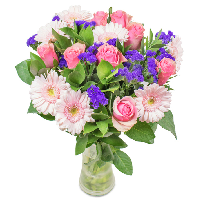 A radiant, expertly arranged floral display from Becontree Heath, this bouquet stands resplendent in a clear glass vase, its vibrant palette singing against the background. The centrepiece includes seven to nine perfectly formed pink roses-some still coyly furled, others just beginning to open, their classic spirals promising timeless romance and affection. Five to seven pale pink gerbera daisies accompany them, their large, radiant faces edged with petals that transition from soft blush to almost ivory, each delicate centre glowing under natural light-much like the blooms one might encounter near Mayesbrook Park in the spring. Interspersed among the focal flowers are vivid clusters of purple statice, lending an intriguing depth and lively contrast. The arrangement is enriched with an abundance of lush green foliage, each leaf fresh, textural, and striking, serving as a verdant base that accentuates the bouquet's energy. Visible stems and water in the vase complete the natural aesthetic, enhancing the sense of newly delivered freshness from a trusted Becontree Heath florist. Perfect for birthdays, anniversaries, Mother's Day, or a warm message to someone dear, this bouquet expresses joy, celebration, and genuine local affection in every carefully crafted detail.